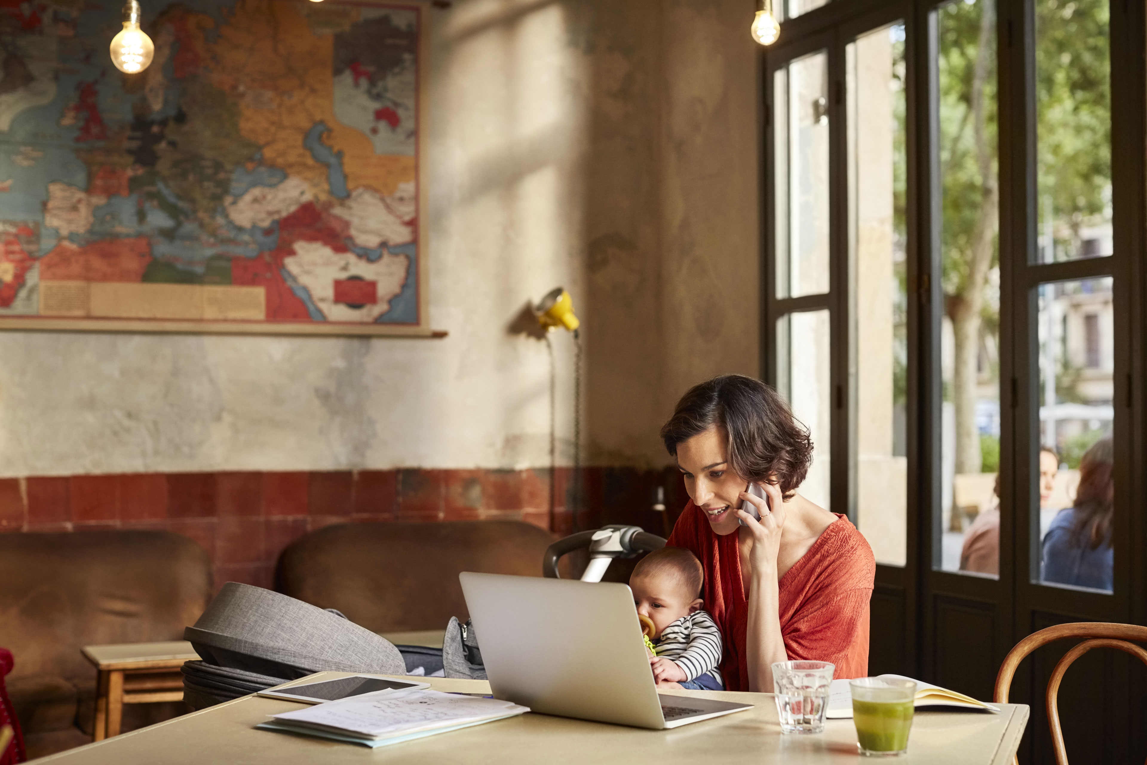 young-woman-on-the-phone-looking-at-laptop-holding-baby